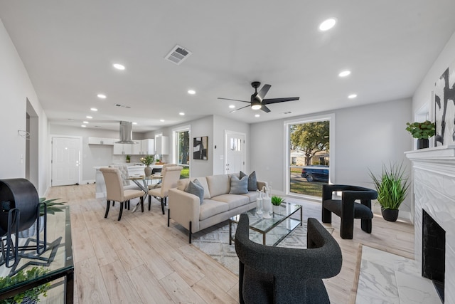 living room with ceiling fan, a premium fireplace, and light hardwood / wood-style floors