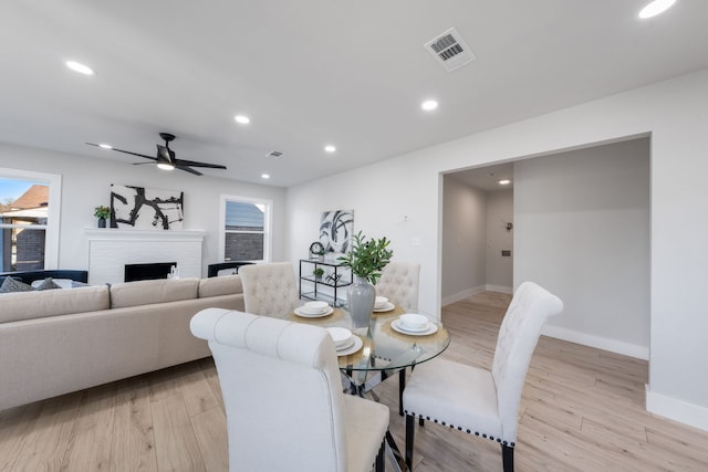 dining room with ceiling fan, light wood-type flooring, and a brick fireplace