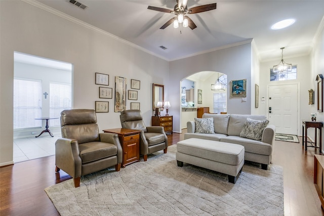 living room with light wood-type flooring, ornamental molding, and ceiling fan with notable chandelier