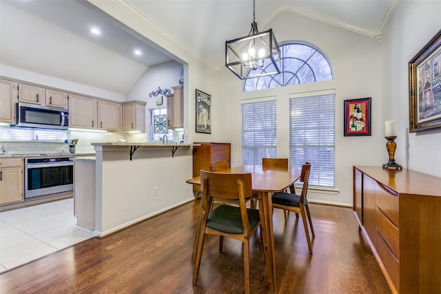 dining room with a healthy amount of sunlight, a notable chandelier, light wood-type flooring, lofted ceiling, and crown molding