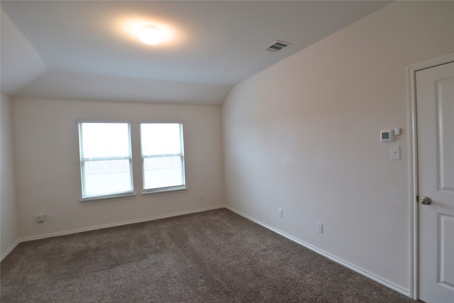 spare room with baseboards, visible vents, vaulted ceiling, and dark colored carpet