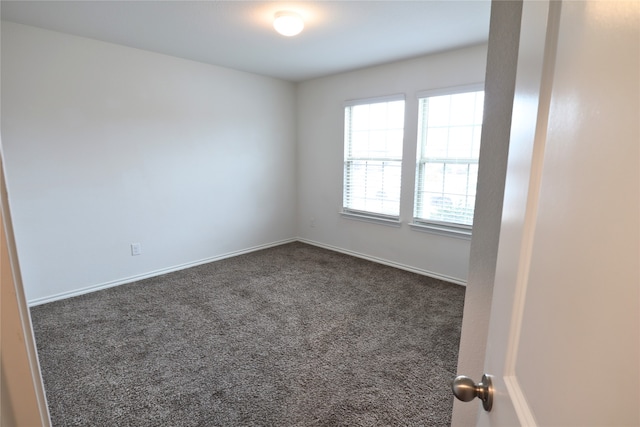 unfurnished room featuring dark colored carpet and baseboards