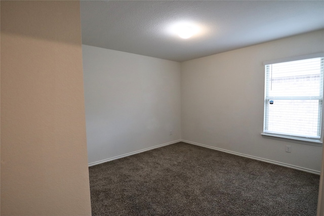 spare room with dark colored carpet and baseboards