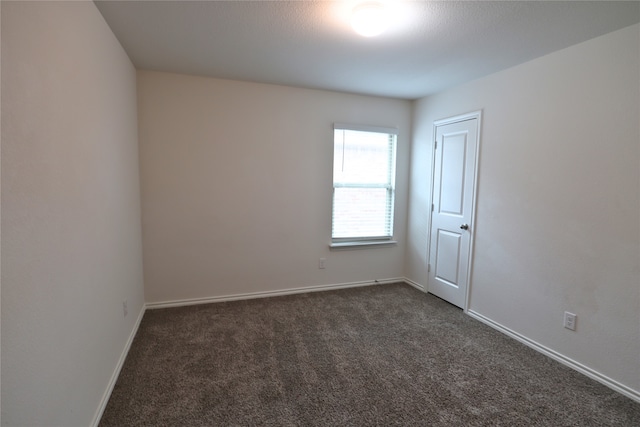 empty room featuring dark colored carpet and baseboards