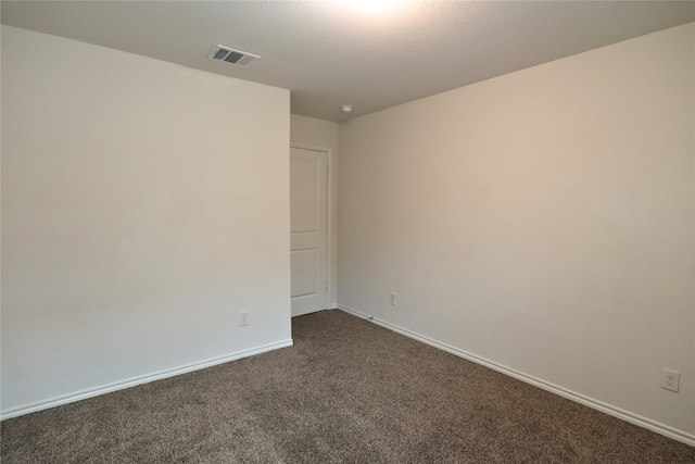 spare room with dark colored carpet, visible vents, and baseboards