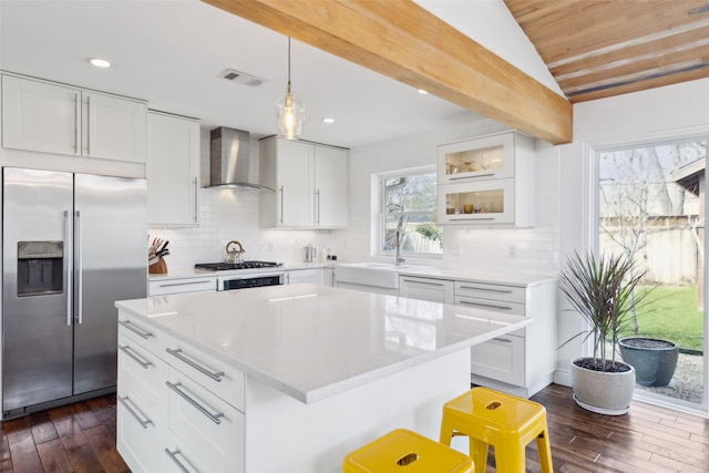 kitchen with wall chimney exhaust hood, white cabinets, a center island, a breakfast bar, and stainless steel appliances