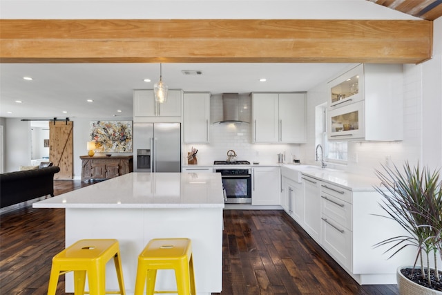 kitchen with wall chimney range hood, stainless steel appliances, a barn door, and white cabinets