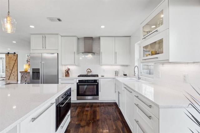 kitchen with decorative light fixtures, sink, white cabinets, wall chimney range hood, and stainless steel appliances