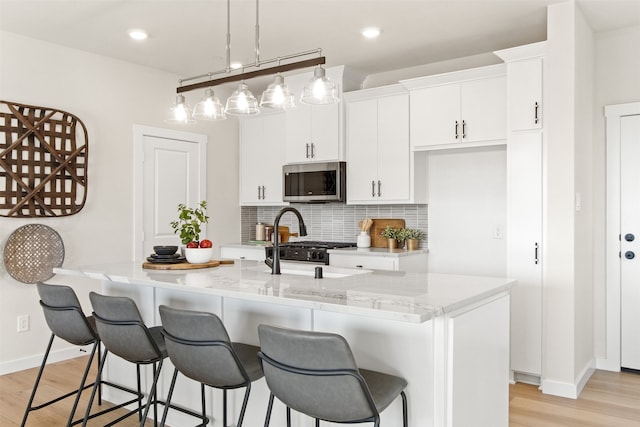 kitchen featuring a center island with sink, hanging light fixtures, light hardwood / wood-style flooring, white cabinets, and decorative backsplash