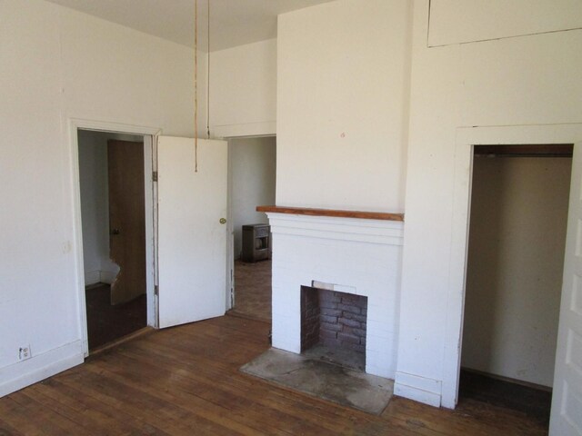 unfurnished living room featuring a brick fireplace and dark wood-type flooring