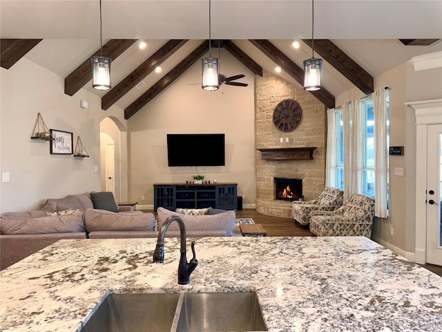 kitchen featuring hanging light fixtures, light stone countertops, sink, and a stone fireplace