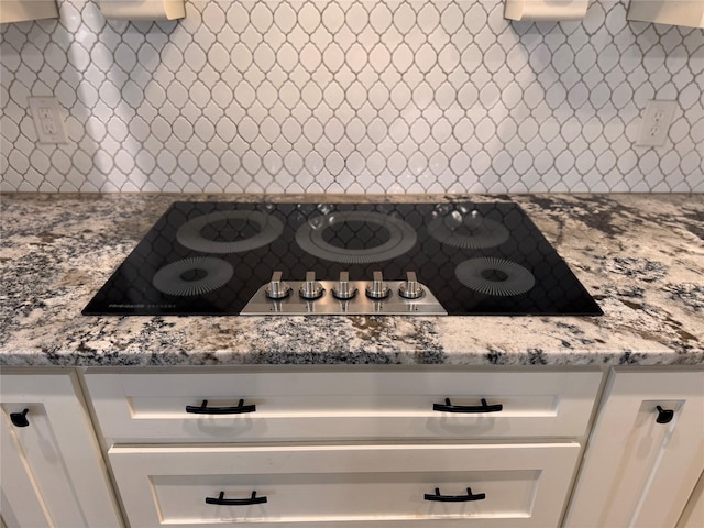 interior space featuring backsplash, light stone countertops, white cabinetry, and black electric stovetop