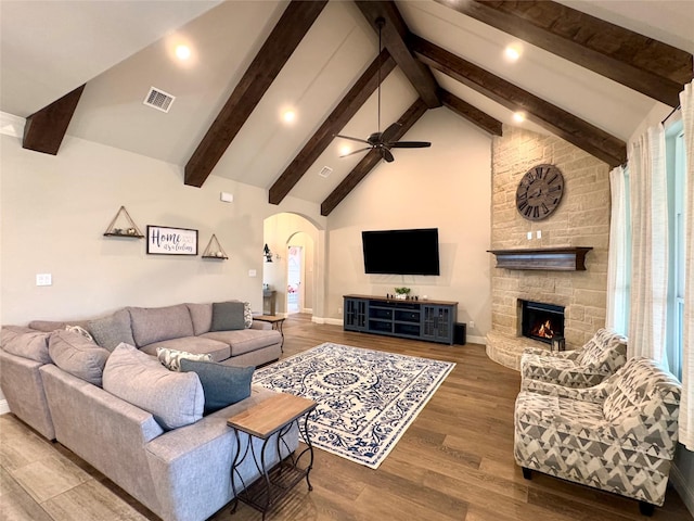 living room with a stone fireplace, ceiling fan, high vaulted ceiling, hardwood / wood-style flooring, and beam ceiling