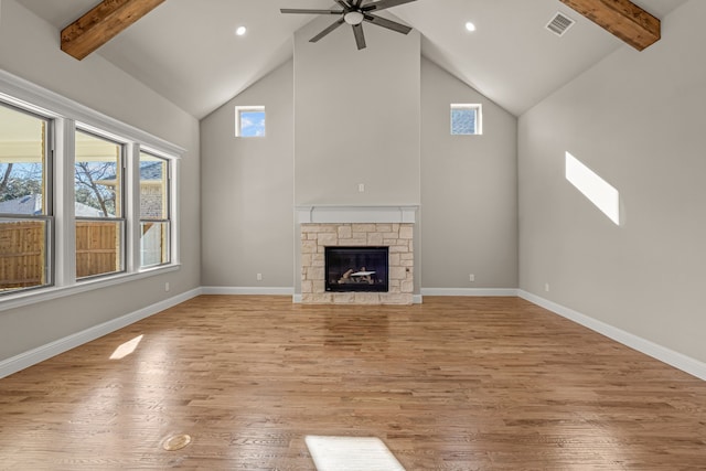 unfurnished living room with high vaulted ceiling, beam ceiling, a stone fireplace, and light hardwood / wood-style floors