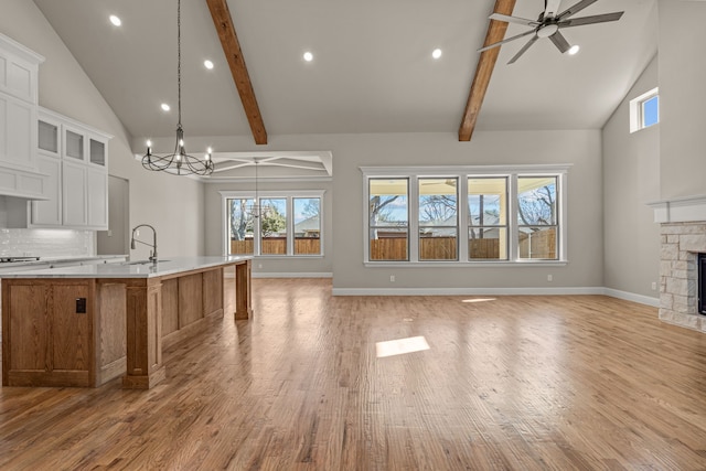 kitchen featuring a stone fireplace, white cabinetry, a spacious island, tasteful backsplash, and decorative light fixtures