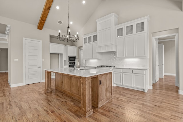 kitchen featuring tasteful backsplash, high vaulted ceiling, beam ceiling, a kitchen island with sink, and white cabinets