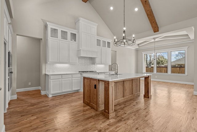 kitchen with a kitchen island with sink, hanging light fixtures, beamed ceiling, and white cabinets