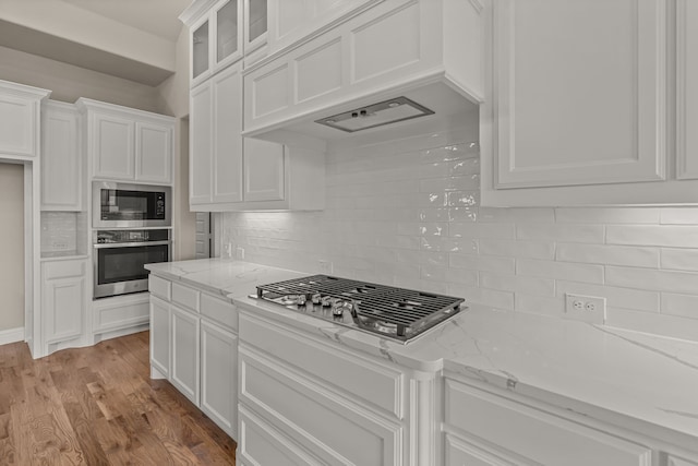 kitchen featuring white cabinetry, stainless steel appliances, custom range hood, and light stone counters