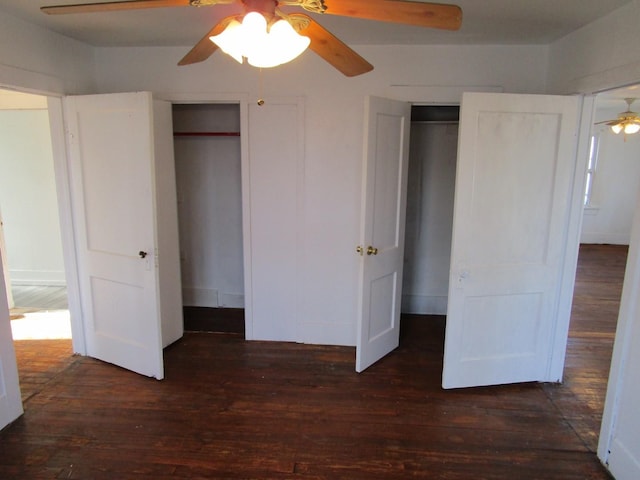 unfurnished bedroom with ceiling fan, dark wood-type flooring, and multiple closets