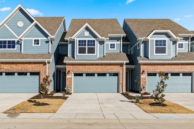 view of front of house featuring a shingled roof, concrete driveway, brick siding, and an attached garage