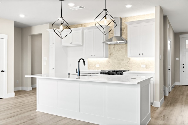 kitchen with a kitchen island with sink, light countertops, a sink, and wall chimney range hood