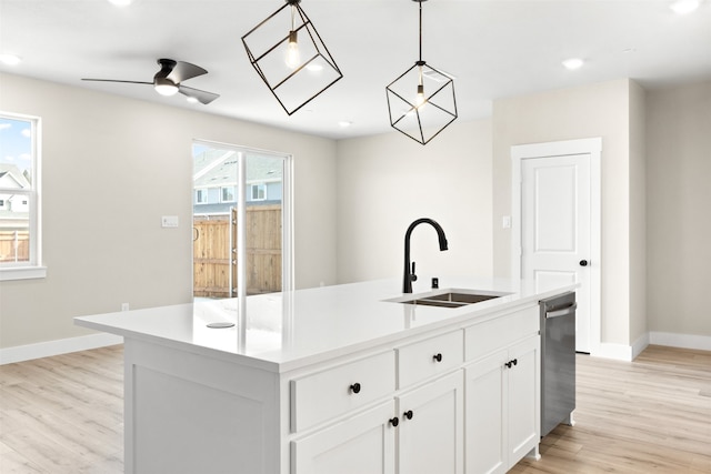 kitchen with decorative light fixtures, a sink, white cabinetry, light countertops, and a center island with sink