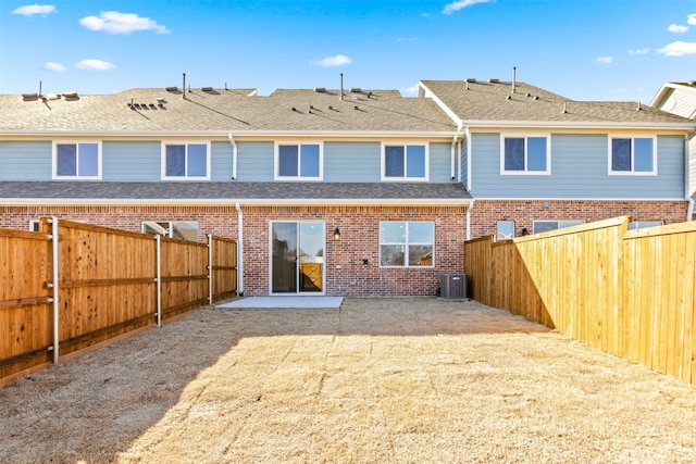 back of house with a shingled roof, a patio, a fenced backyard, cooling unit, and brick siding