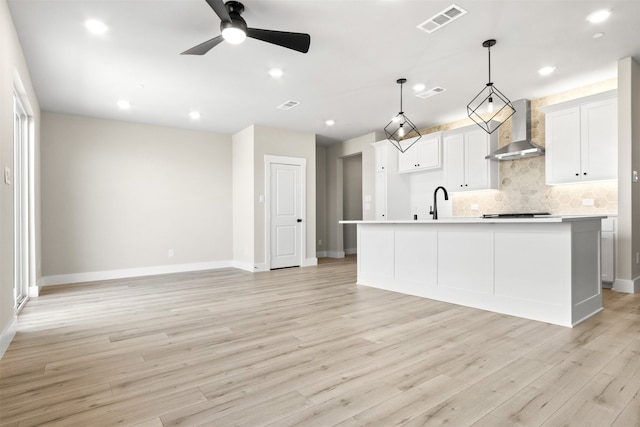 kitchen featuring decorative light fixtures, visible vents, light countertops, an island with sink, and wall chimney exhaust hood