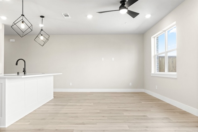 interior space with a ceiling fan, visible vents, light wood-style flooring, and baseboards