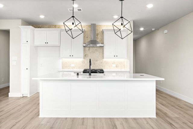 kitchen with an island with sink, wall chimney range hood, and decorative light fixtures