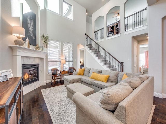 living room featuring dark wood-type flooring, ceiling fan, a fireplace, and a towering ceiling