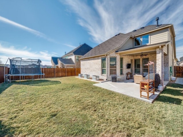 rear view of house with a trampoline, a yard, and a patio