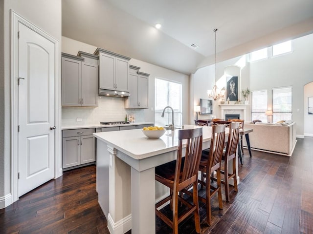 kitchen with a breakfast bar, pendant lighting, gray cabinetry, and a kitchen island with sink