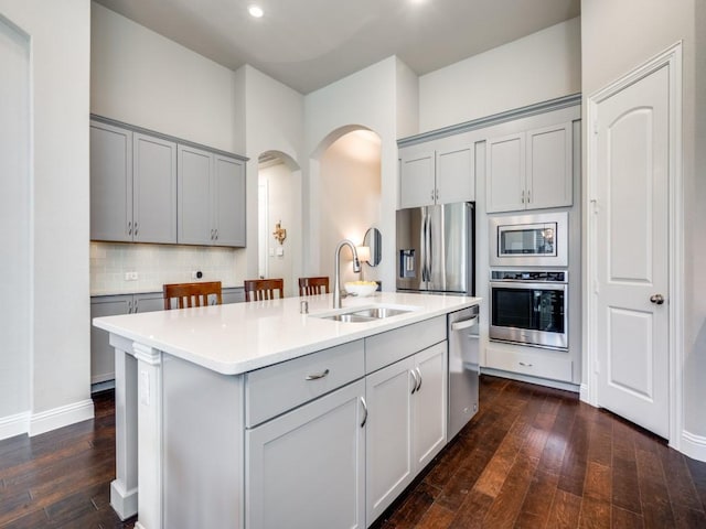 kitchen featuring tasteful backsplash, sink, a kitchen island with sink, gray cabinetry, and stainless steel appliances