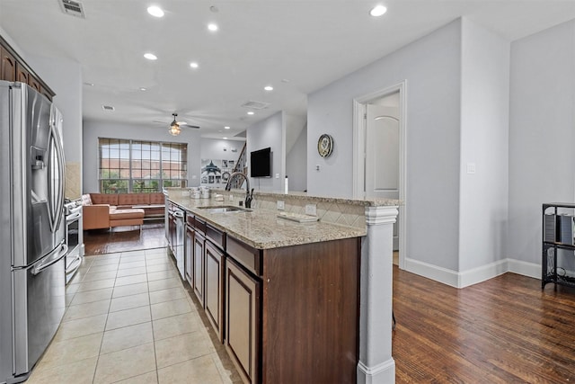 kitchen featuring ceiling fan, sink, a kitchen island with sink, stainless steel appliances, and dark brown cabinets