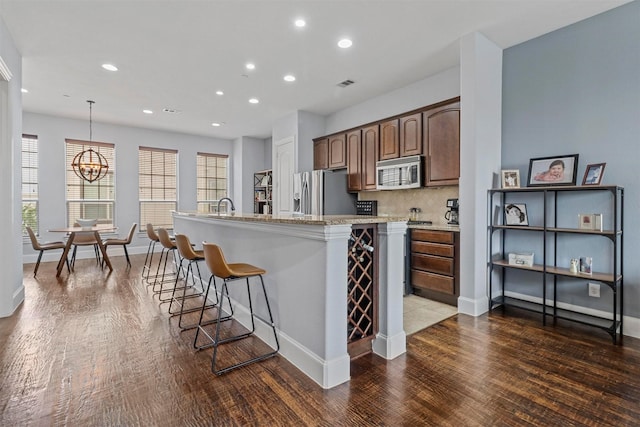 kitchen with pendant lighting, appliances with stainless steel finishes, a kitchen island with sink, a chandelier, and a breakfast bar