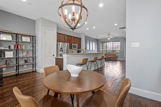 dining area with dark wood-type flooring, sink, and ceiling fan with notable chandelier