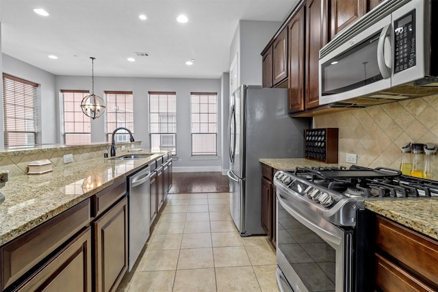 kitchen with light stone countertops, pendant lighting, stainless steel appliances, sink, and a chandelier