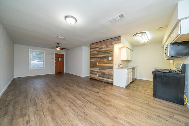 kitchen with white cabinetry, wooden walls, appliances with stainless steel finishes, light hardwood / wood-style flooring, and sink