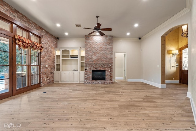 unfurnished living room featuring light hardwood / wood-style floors, ceiling fan, a brick fireplace, brick wall, and crown molding