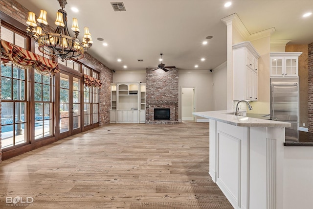 kitchen with white cabinetry, a fireplace, ornamental molding, ceiling fan with notable chandelier, and stainless steel built in refrigerator