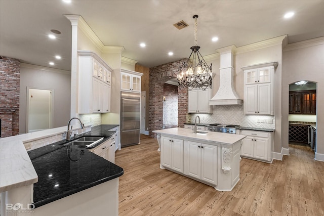 kitchen with decorative light fixtures, custom exhaust hood, sink, a kitchen island with sink, and stainless steel appliances