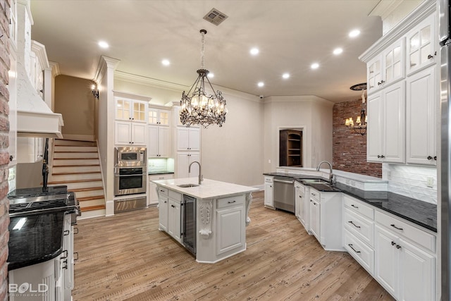 kitchen with a center island with sink, appliances with stainless steel finishes, tasteful backsplash, decorative light fixtures, and white cabinets