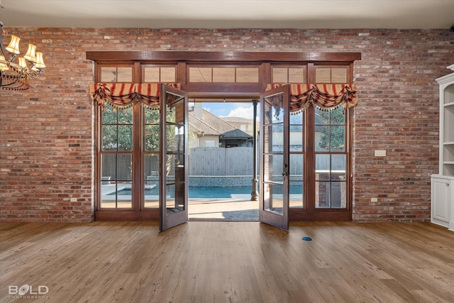 doorway with hardwood / wood-style flooring, brick wall, and french doors