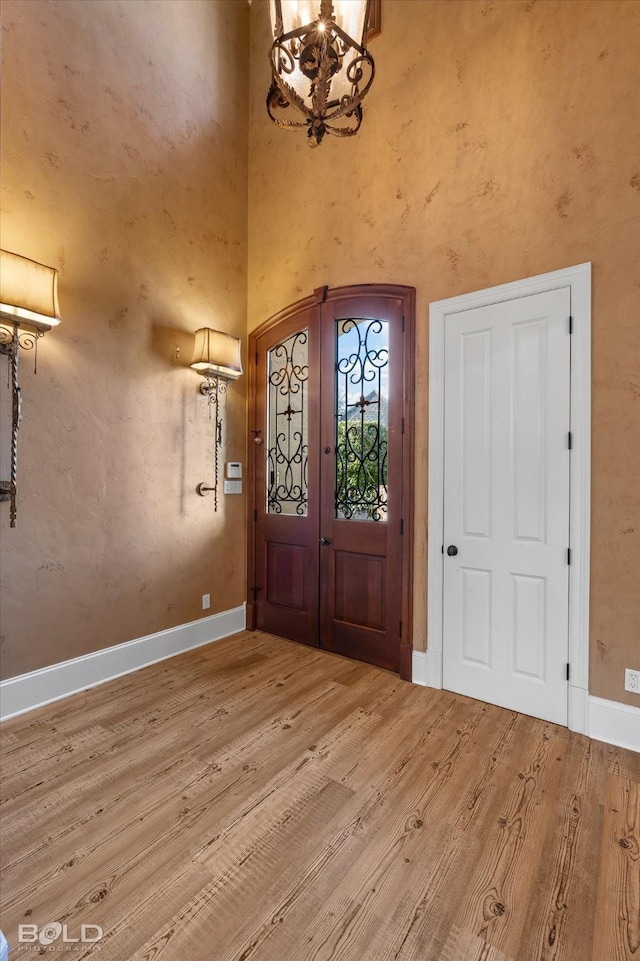 entryway with a towering ceiling, a notable chandelier, french doors, and light wood-type flooring