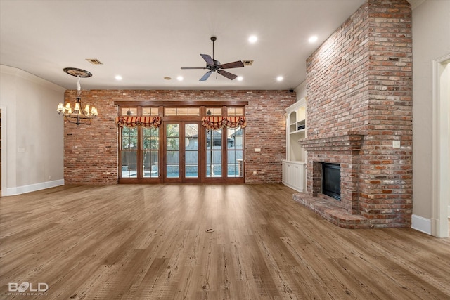 unfurnished living room featuring wood-type flooring, a fireplace, ceiling fan with notable chandelier, and ornamental molding