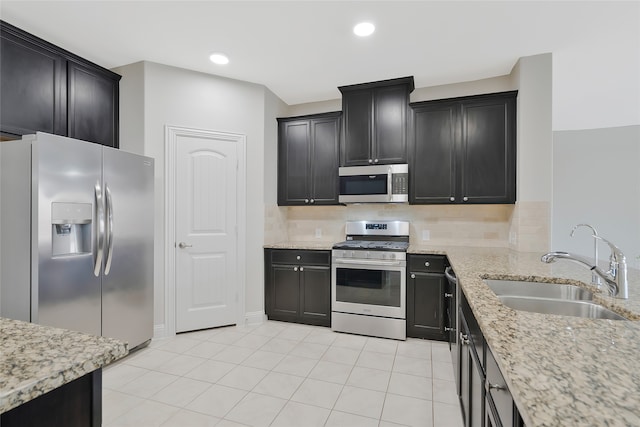 kitchen with stainless steel appliances, backsplash, light stone counters, and sink