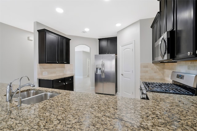 kitchen featuring light stone countertops, backsplash, appliances with stainless steel finishes, and sink