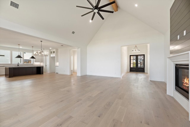 unfurnished living room with light wood-type flooring, beam ceiling, and high vaulted ceiling