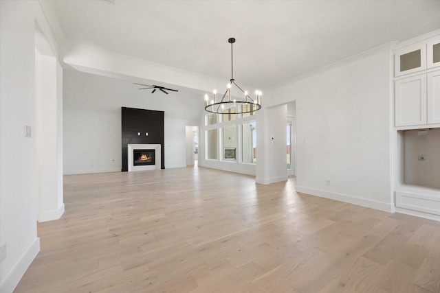 unfurnished living room with ceiling fan with notable chandelier, a large fireplace, ornamental molding, and light wood-type flooring